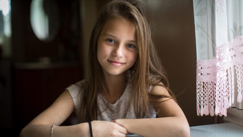 Portrait of cute ten-year-old girl posing for the camera sitting at the table.