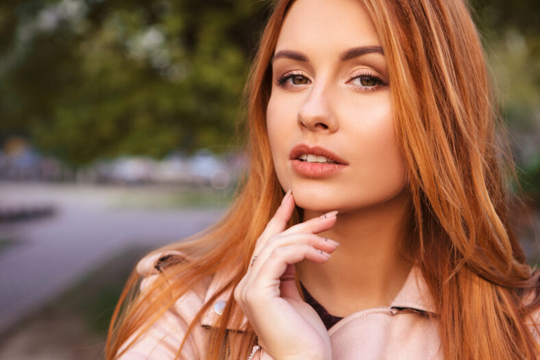 Red haired plus size woman walking on a park. Cold weather, she wears leather jacket. Emotional portrait
