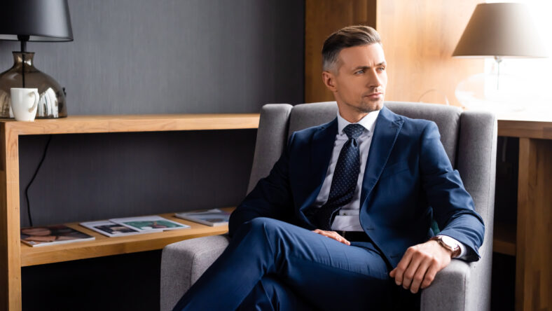handsome businessman in suit sitting in armchair and looking away