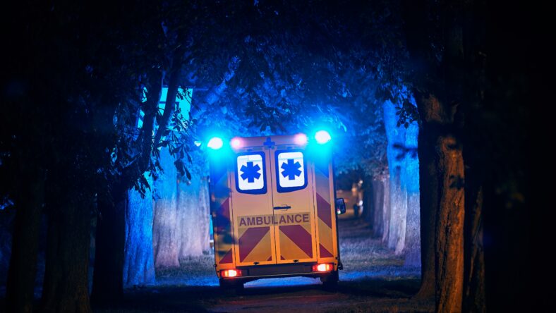 Rear view of ambulance of emergency medical service against dark alley. Themes rescue, hope and health care.