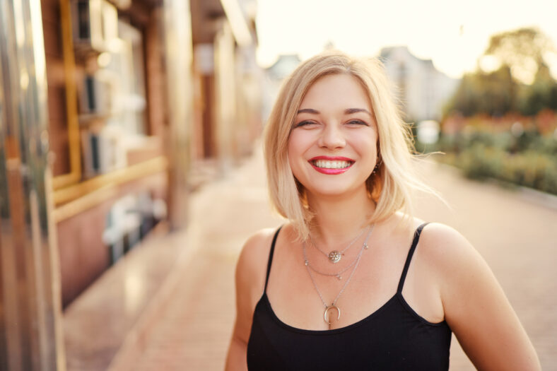 Outdoor portrait of happy young woman walking by city street.