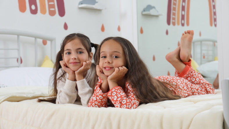 Cute girls in pajamas on bed at home