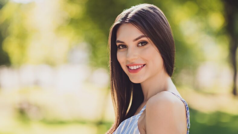 Portrait of gorgeous cheerful good looking female with long brunette hair enjoying free time outdoors walk summer weather.
