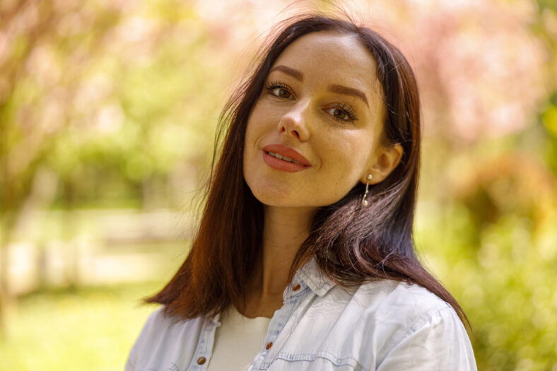 Portrait of beautiful young brunette woman looking and smiling to camera. At park. Close up.