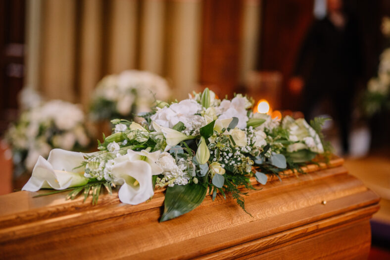 A coffin decorated with many flowers and candles in a beautiful church, ceremony