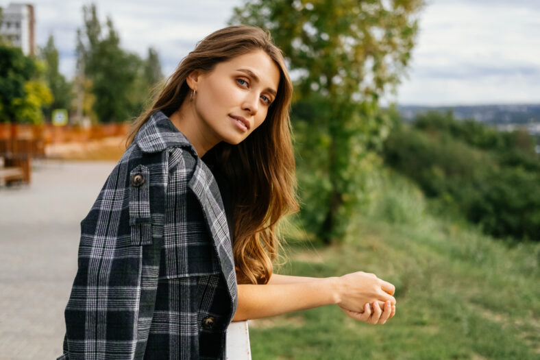 Beautiful woman is looking mysteriously at the camera while leaning on railing in a park.