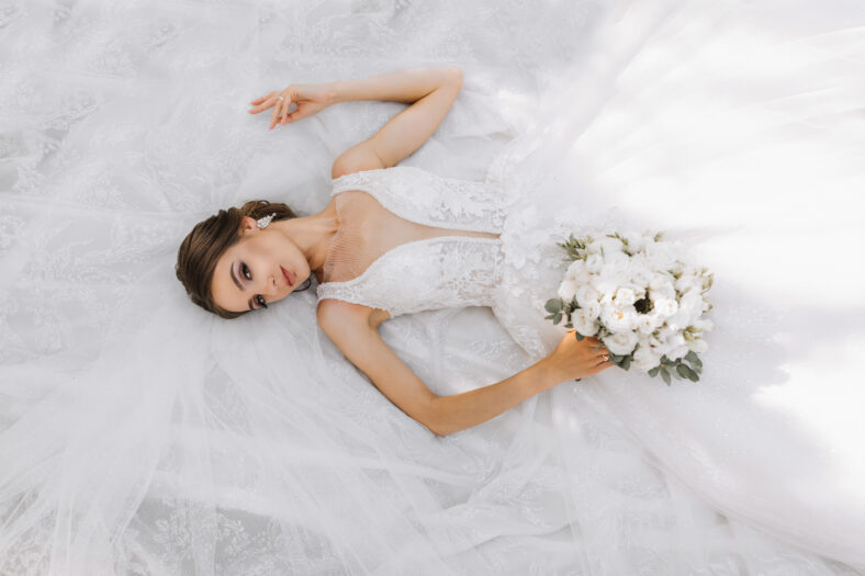 Beautiful bride with wedding bouquet of flowers, attractive woman in wedding dress. The bride dreamily lies on her dress, the photo is taken from above
