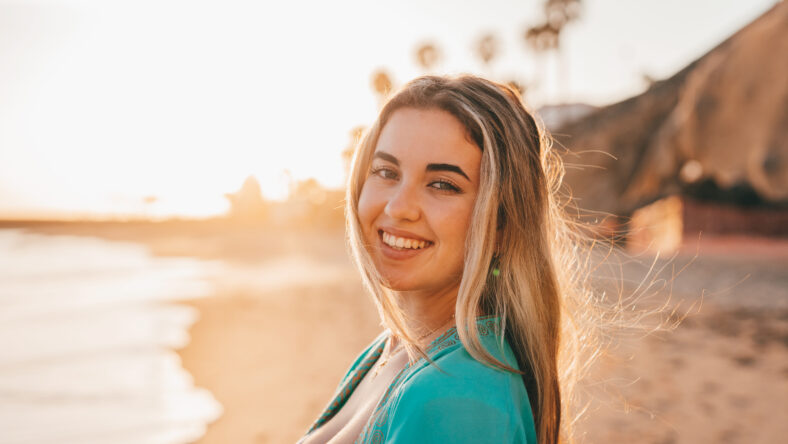 Portrait of one happy beautiful woman on the sand of the beach enjoying and having fun at the sunset of the day. Looking at the camera smiling.
