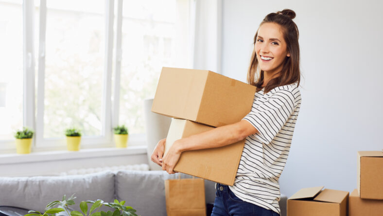 Young woman moving into new apartment holding cardboard boxes with belongings