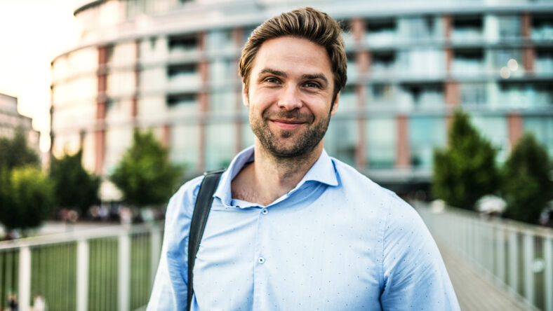 A portrait of a handsome young businessman with a bag walking on a bridge.