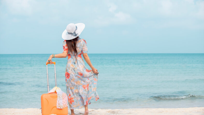 Relax traveler woman in dress with sun hat holding suitcase standing on the beach enjoys her tropical vacation , lifestyle holiday travel summer concept