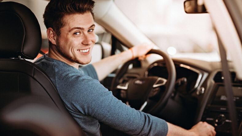 Happy young driver behind the wheel of a car. Buying a car and driving concept
