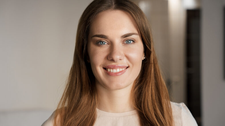 Young woman with beautiful perfect skin giving smile to camera. Happy student or freelance worker headshot portrait selective focus. Fashion, beauty, natural make-up and youth concept