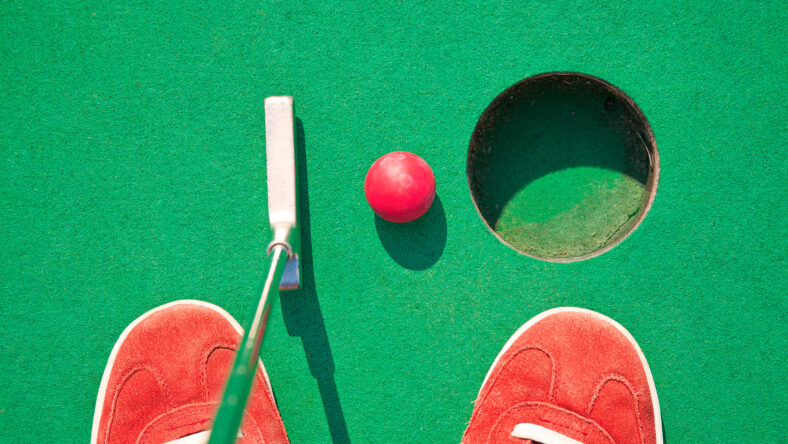 Close-up of miniature golf hole with bat and ball