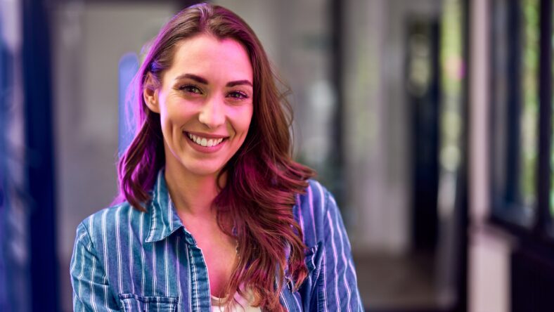 A happy female employee on her first work day, standing at the workplace and smiling for the camera.