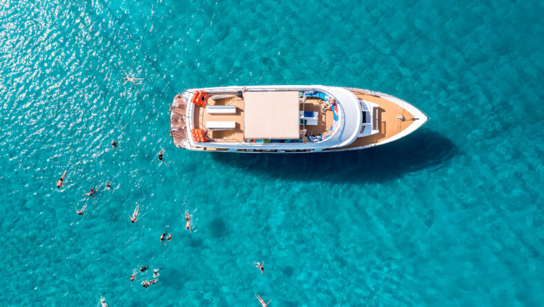 Close-up overhead view of a yacht anchored in the turquoise sea and swimming tourists