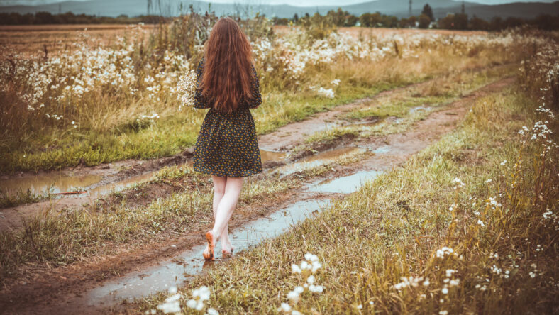girl going on rural road with a bouquet of wild flowers