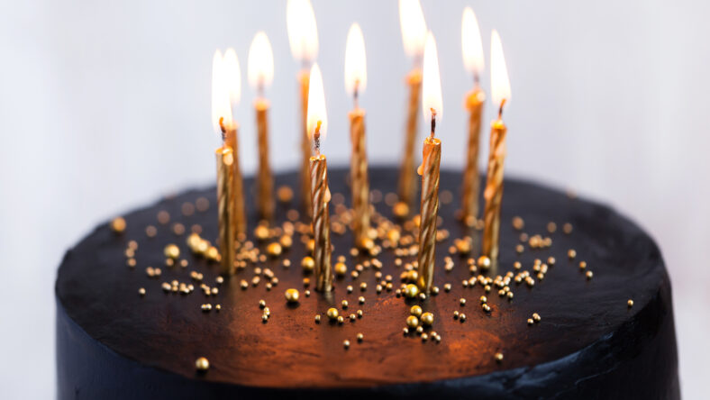 Black round birthday cake with burning golden