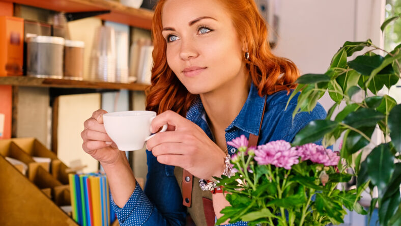 Close up portrait of redhead female barista drinks coffee.