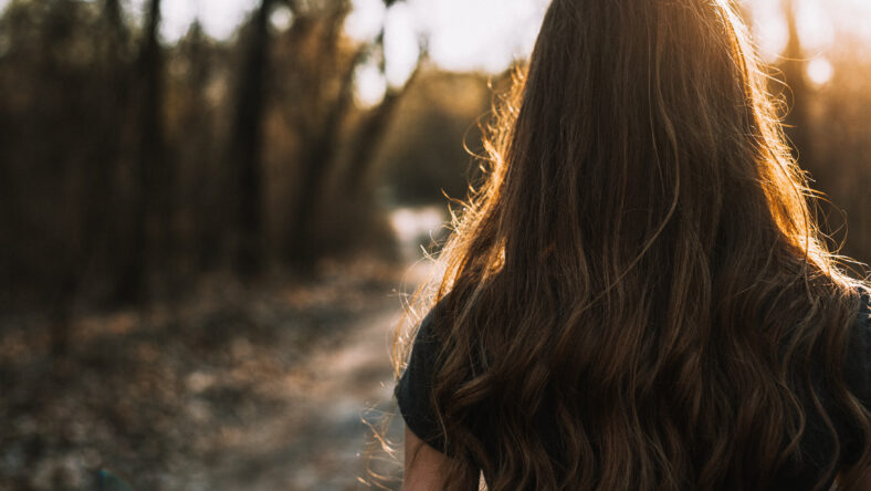 Rear view of sad young woman walking through park at sunset