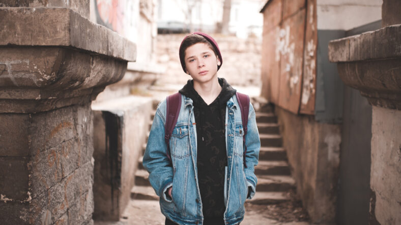 Stylish teen boy 14-16 year old posing at slum street. Sad emotions. Abandoned teenager.