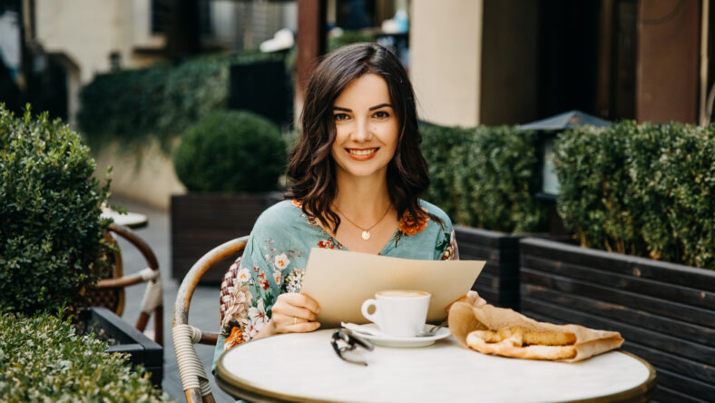 Young happy woman sitting at a cafe terrace, holding a menu.