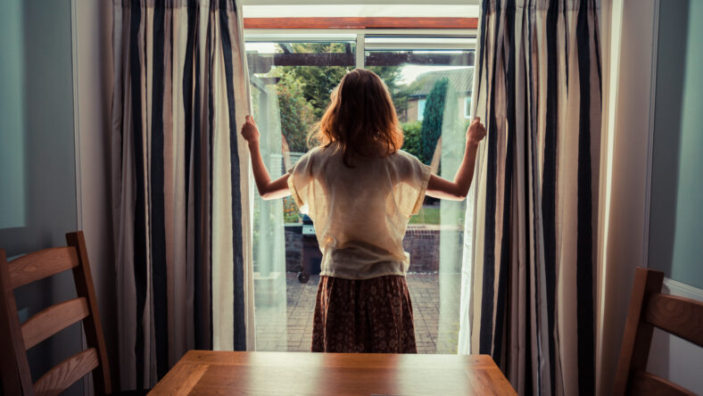 A young woman is opening the curtains at sunrise