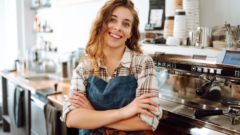 Portrait of a beautiful barista girl in an apron in a modern cafe bar. Startup successful small business owner beauty woman stand in coffee shop restaurant. Business concept.
