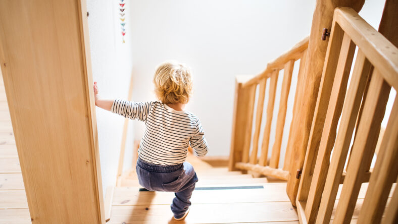 Little toddler walking down the stairs. Domestic accident. Dangerous situation at home. Child safety concept. Rear view.