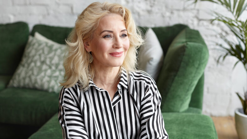 People, rest, leisure, lifestyle and relaxation. Elegant blonde woman pensioner with stylish hairdo and natural make up spending day at home, smiling while reminiscing happy moments of her youth