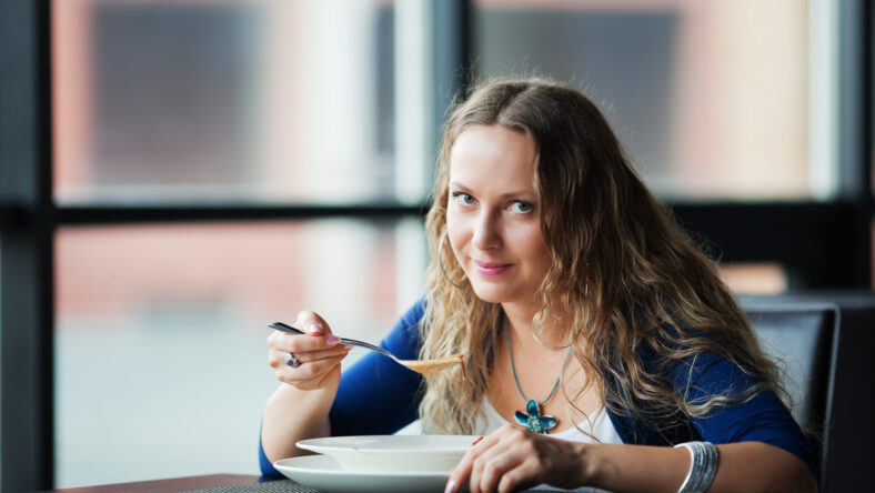 Young woman eating soup at restaurant.