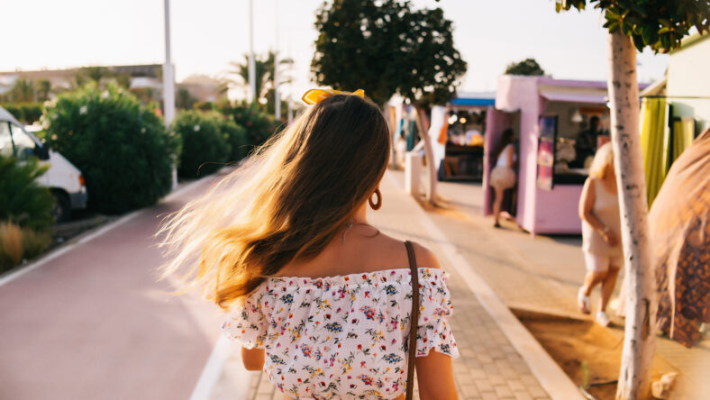 Girl walking back with brown red hair in a light blouse, background sunny spring day, copy space.