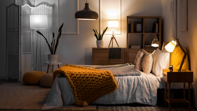 Interior of bedroom with knitted plaid on bed and glowing lamps at night