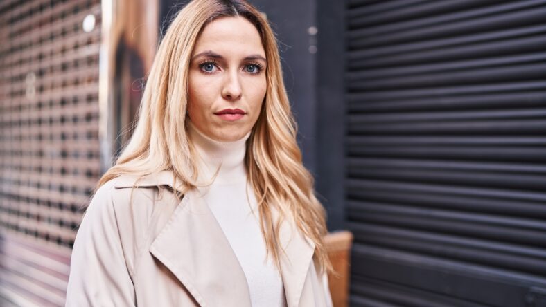 Young blonde woman standing with serious expression at street
