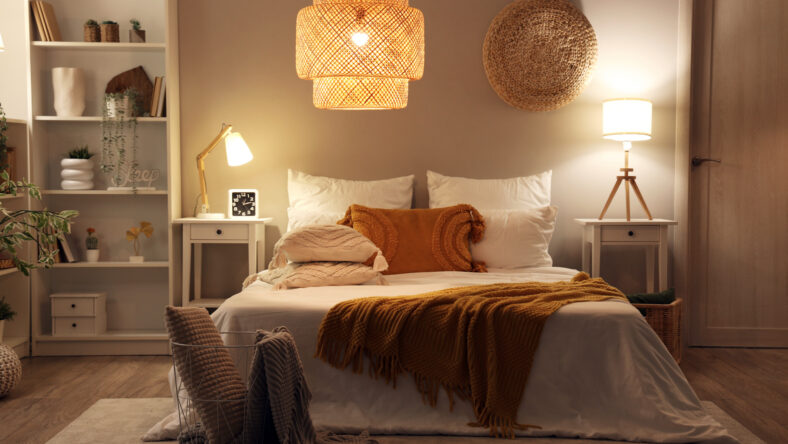 Interior of cozy bedroom with comfortable bed, blanket and glowing lamps at night
