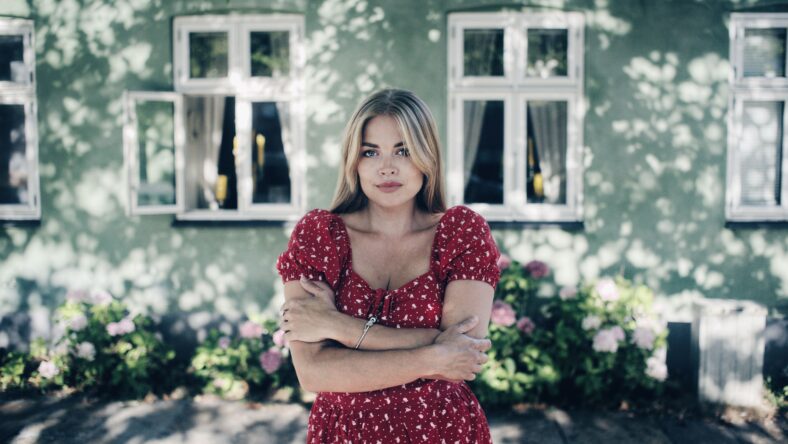 Young blonde female in a red spotted dress posing in front of a house