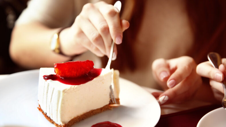 Woman eating tasty cheesecake on table in cafe or restaurant