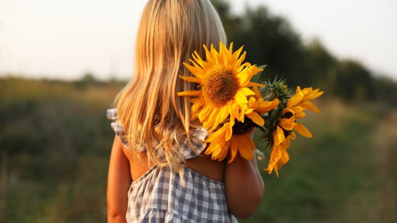 Little girl with sunflowers at meadow, back view. Child enjoying beautiful nature