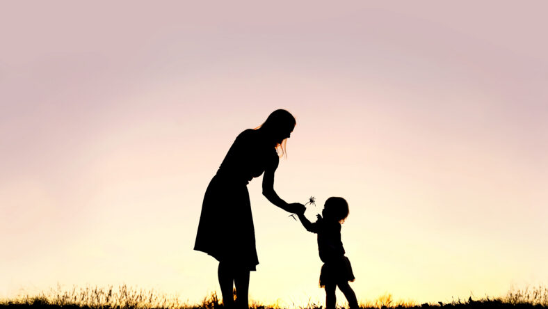 A silhouette of a sweet toddler girl is handing her mother a Daisy flower, in a meadow outside at sunset on a summer day.