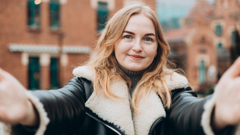 Beautiful woman in good mood looks into camera and takes selfie in the street. Blogging, technology, lifestyle, travel, tourism, active life.