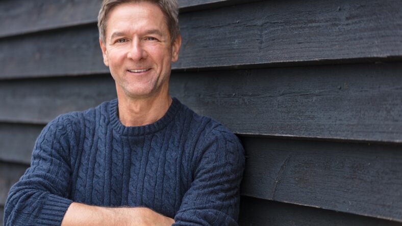 Portrait shot of an attractive, successful and happy middle aged man male arms folded outside wearing a blue sweater