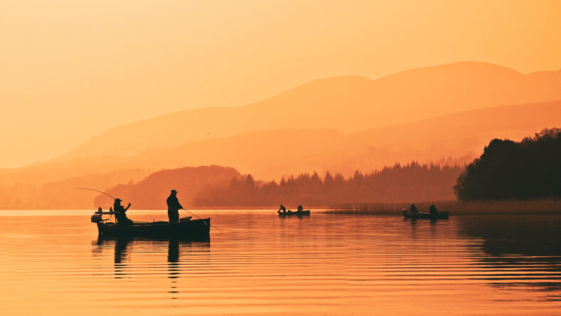 Man fishing on lake from boat at sunset. Lake of Menteith, Stirlingshire, Scotland, UK