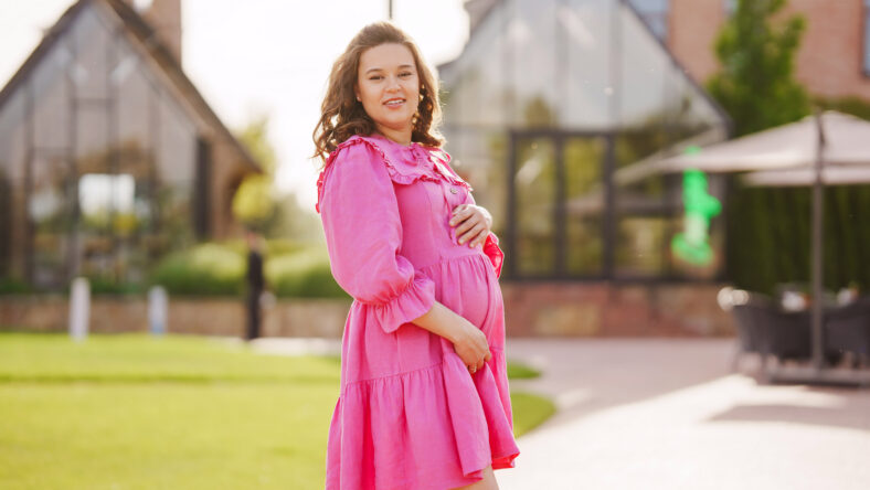 Beautiful and happy pregnant young woman in pink dress on a walk in the park. Long-awaited and healthy pregnancy. clothes and cosmetics for expectant mothers.