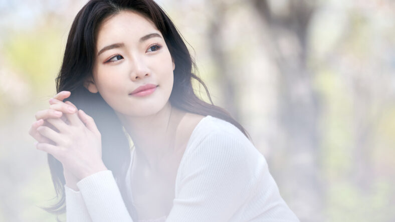 Young Asian female sitting on park bench surrounded by cherry blossoms in spring