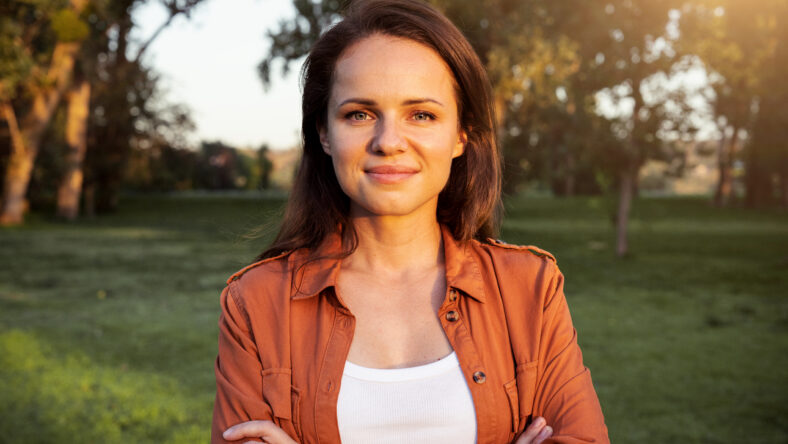 Natural portrait of a young brunette woman with crossed arms outdoors in a park.
