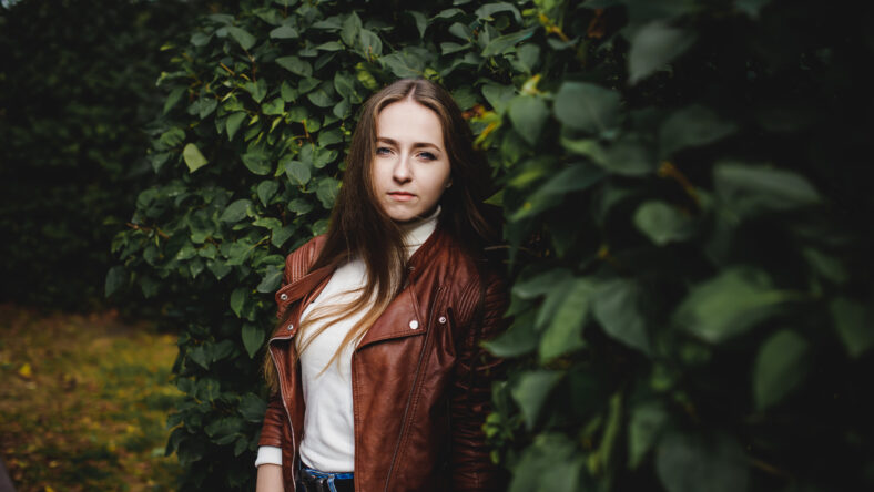 street portrait of a female student in fashionable clothes, blue jeans and a brown jacket, outdoors