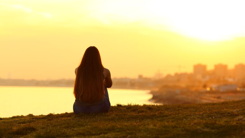 Back view backlight portrait of a single woman watching a sunset on the city with a warm light in the background