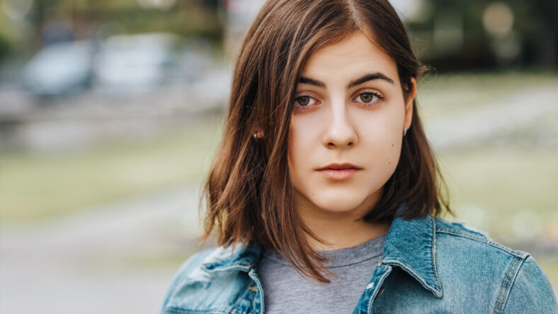 Outdoor portrait of young teenage 16 year old girl, wearing denim jacket