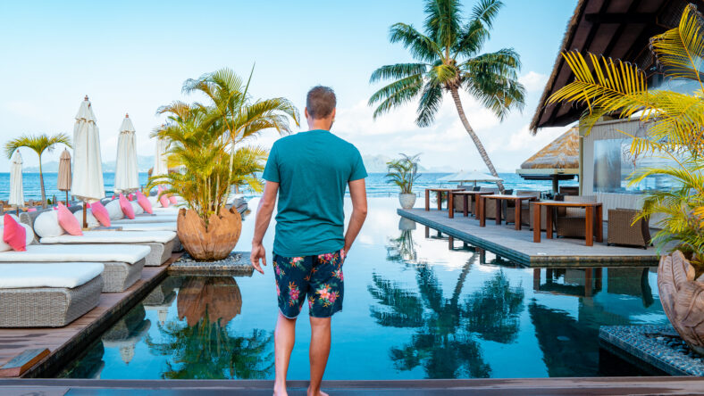 young man in front of an Luxury infinity swimming pool, relaxing holidays vacation in Seychelles islands. La Digue