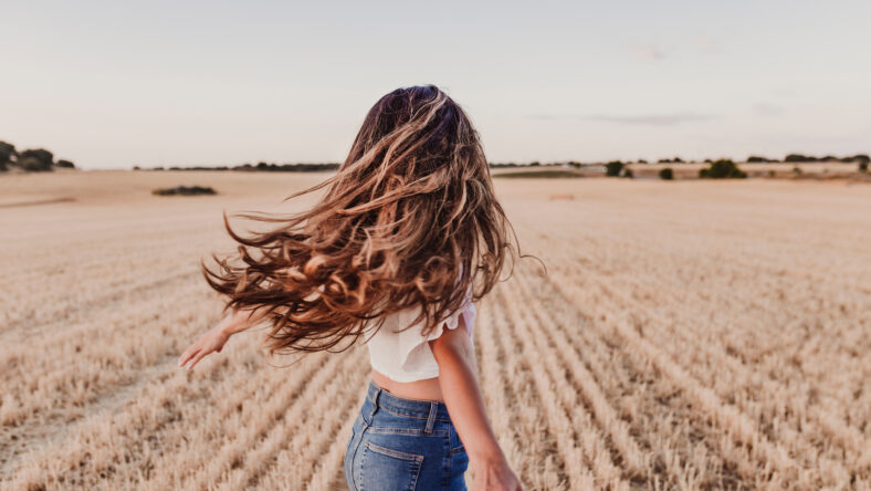 Summer Girl enjoying nature on yellow field. Beautiful young woman dancing Outdoors. Long hair in the wind. Happiness and lifestyle. Back view